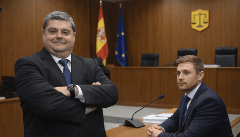 Abogado mercantil en juzgado asesorando a cliente antes de juicio con toga española